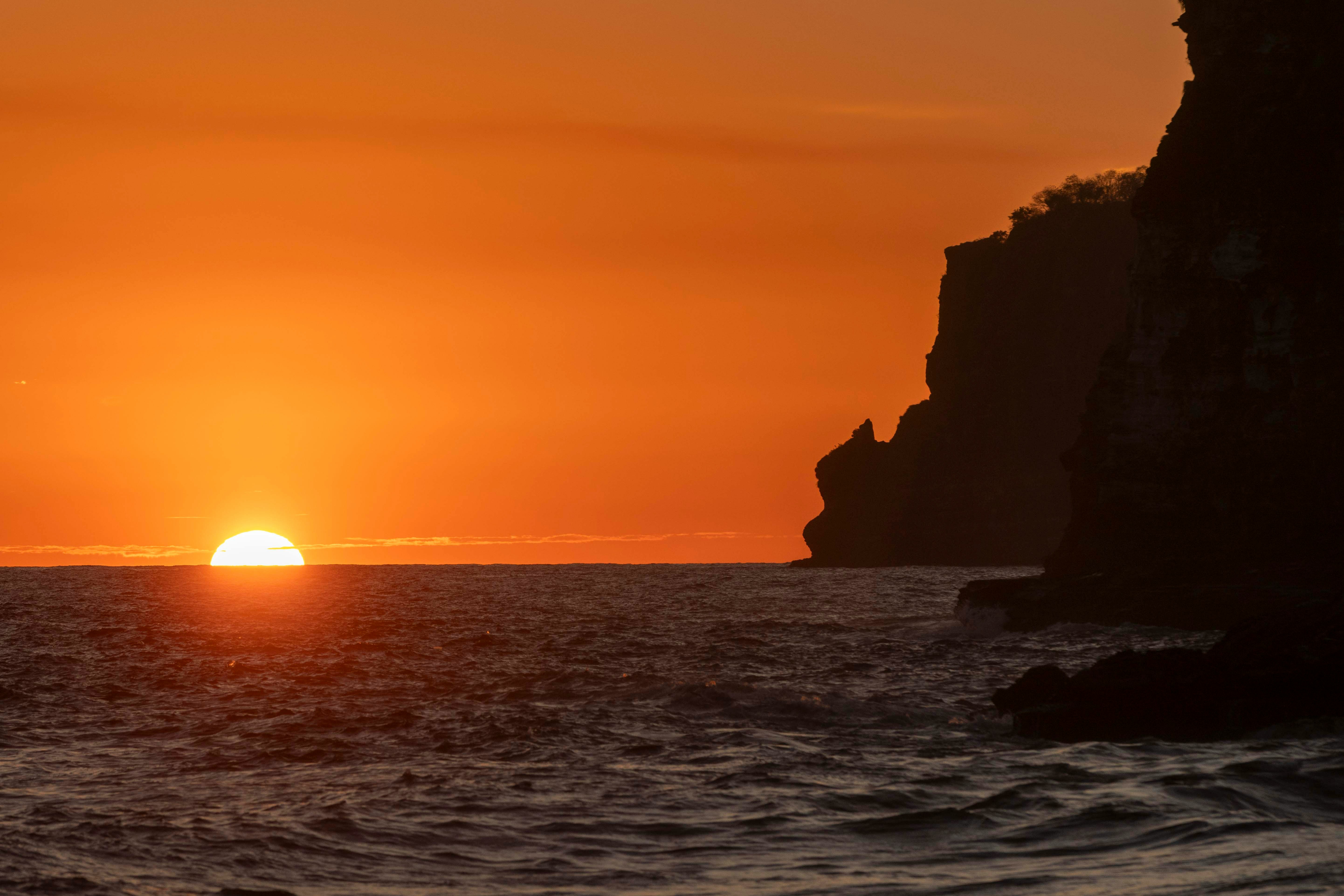 Sunset over the Pacific Ocean with rocky cliff silhouette, Paracas coast Peru
