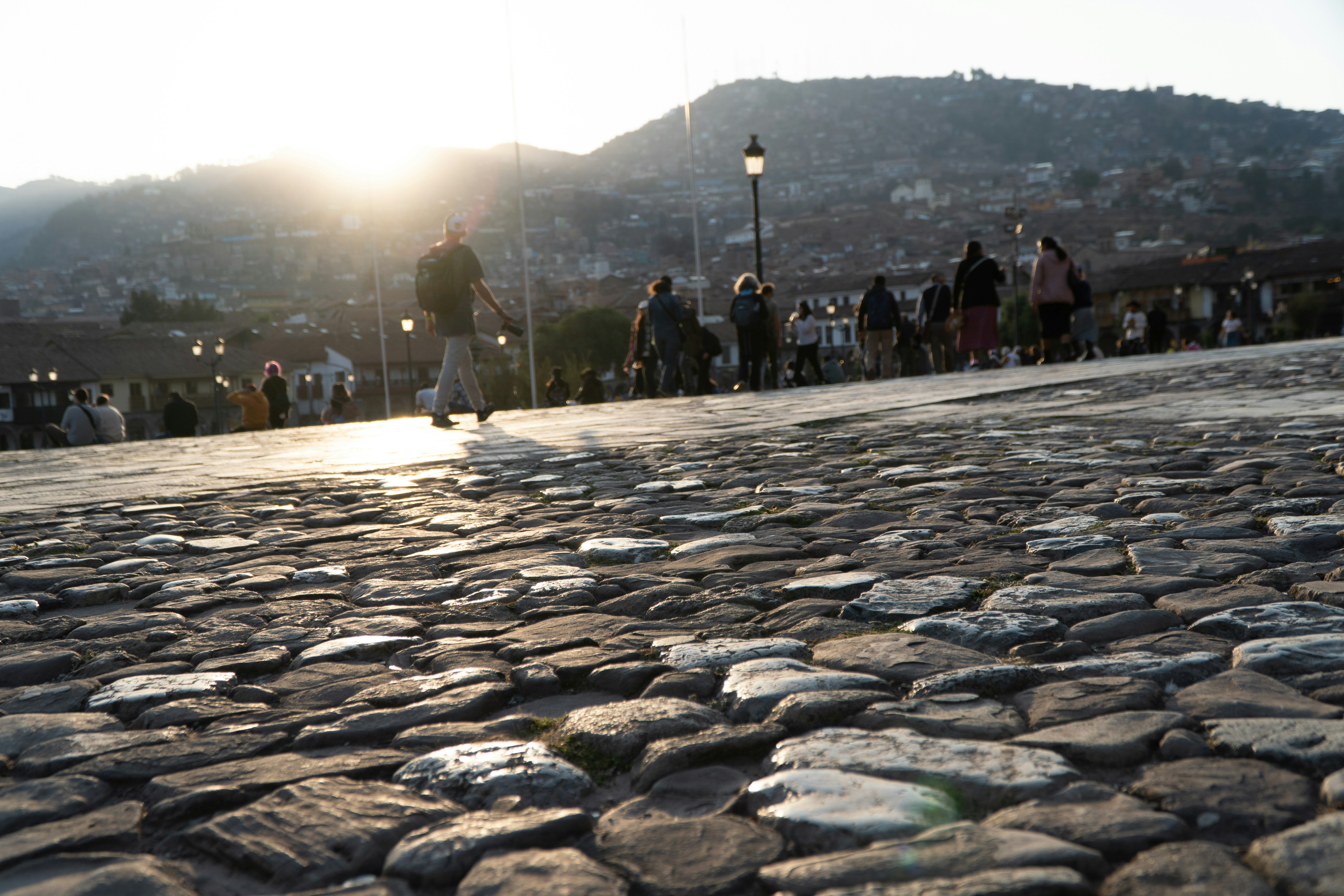 Cobblestone street in Cusco at sunset with city and hills behind, Peru