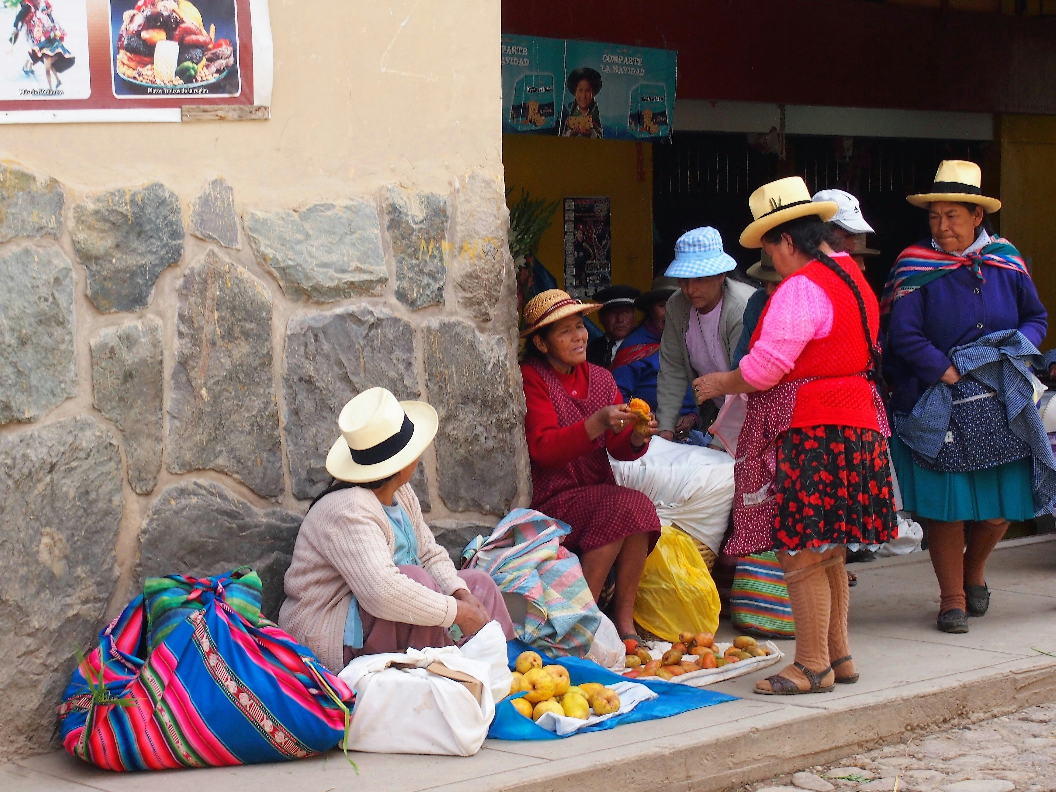 Andean women in hats selling fruit and food on a market street, Sacred Valley, Peru