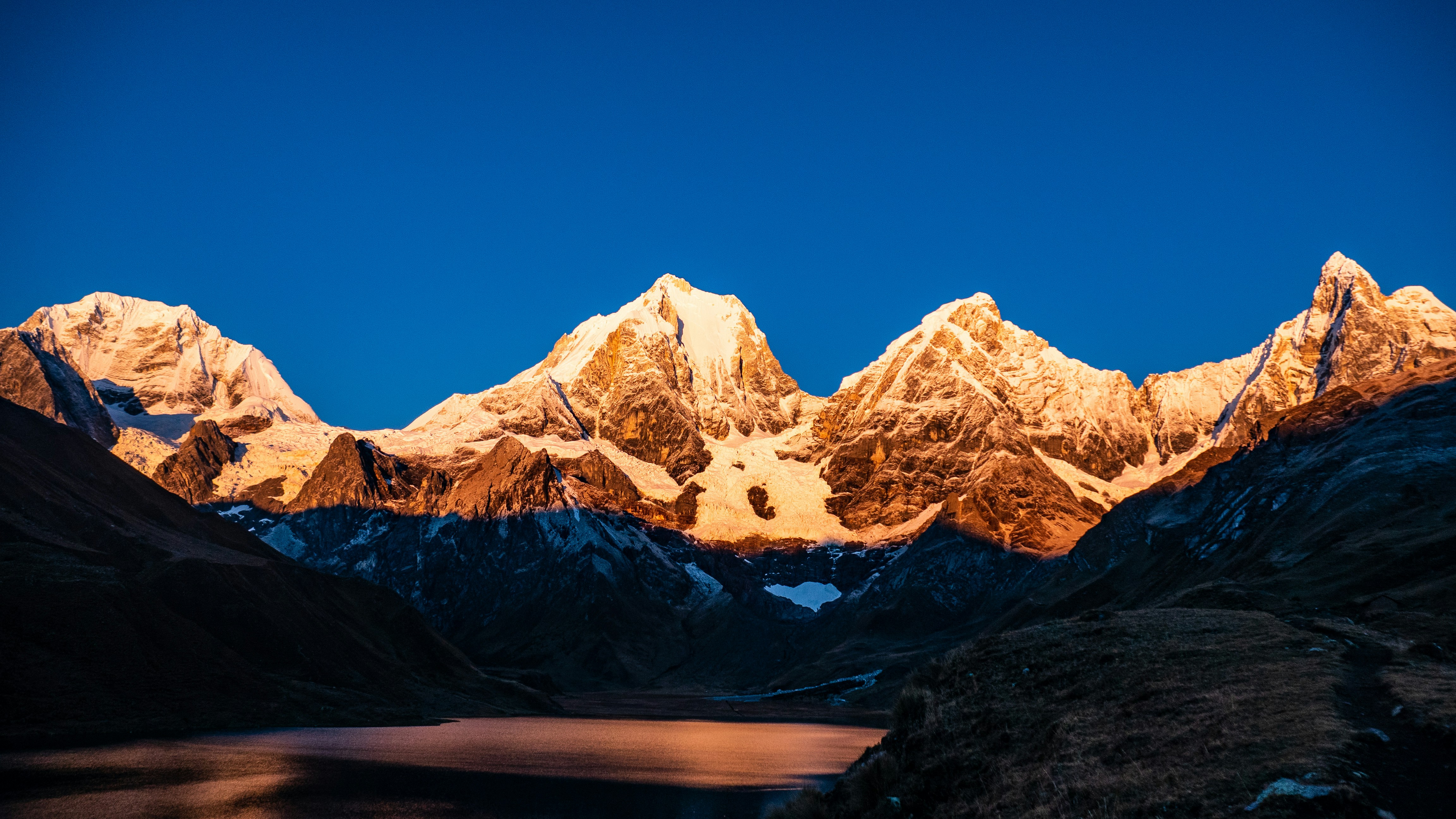 Snow-capped Cordillera Huayhuash peaks glowing at golden hour above a glacial lake, Peru