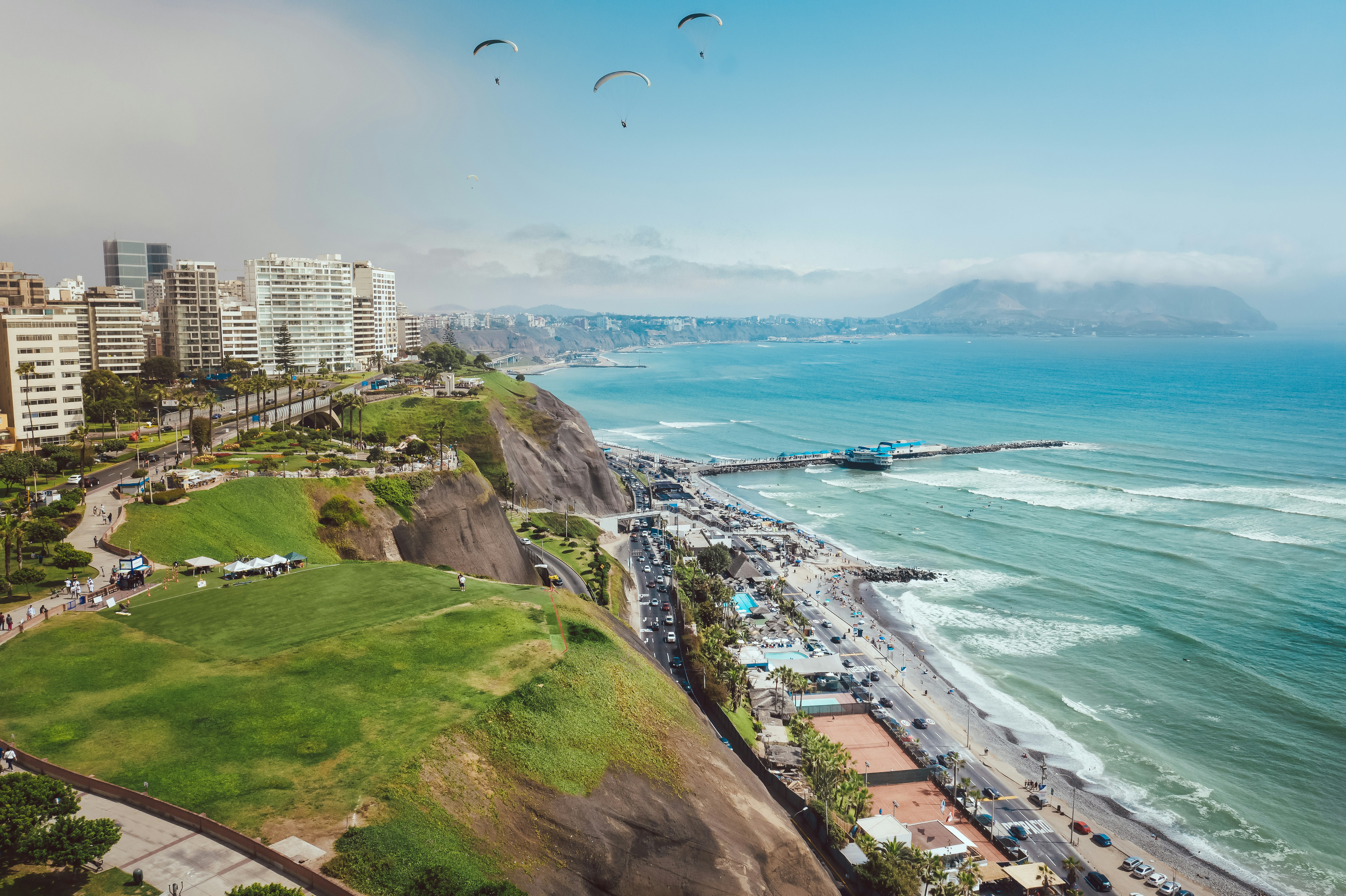 Aerial view of Lima's Miraflores cliffs above the Pacific Ocean with paragliders and pier below