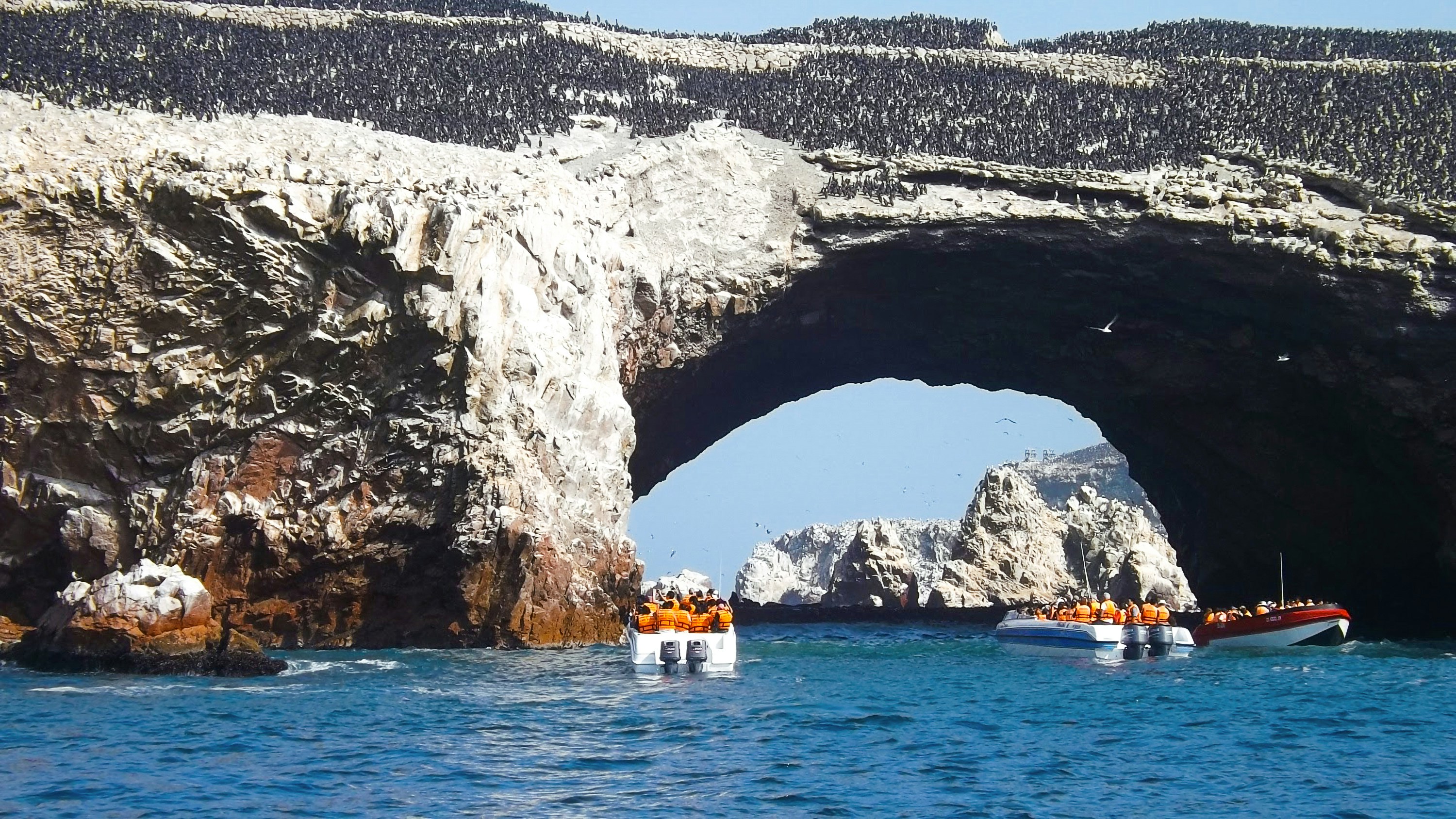 Tour boats passing through a rock arch at the Ballestas Islands, Paracas, Peru