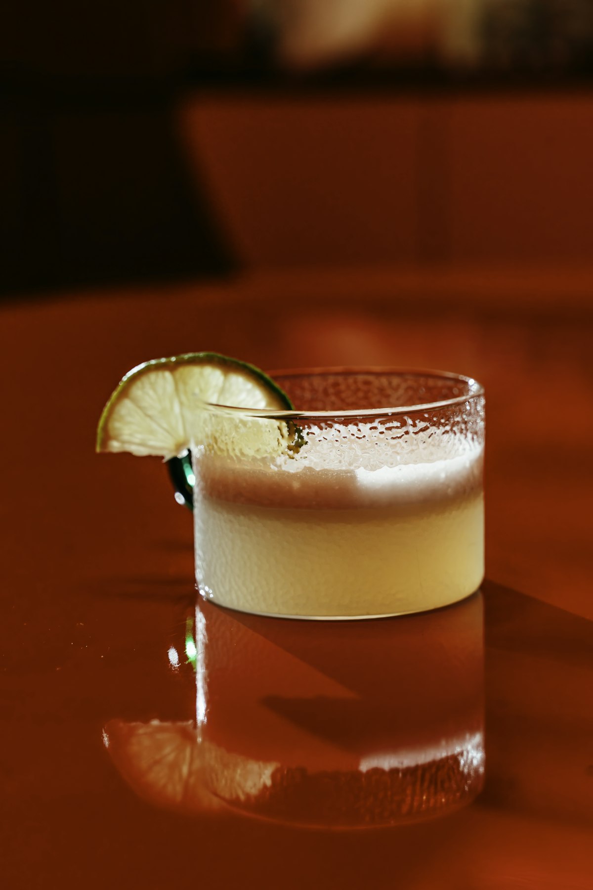 Classic pisco sour cocktail with white egg white foam and lime garnish on dark bar surface