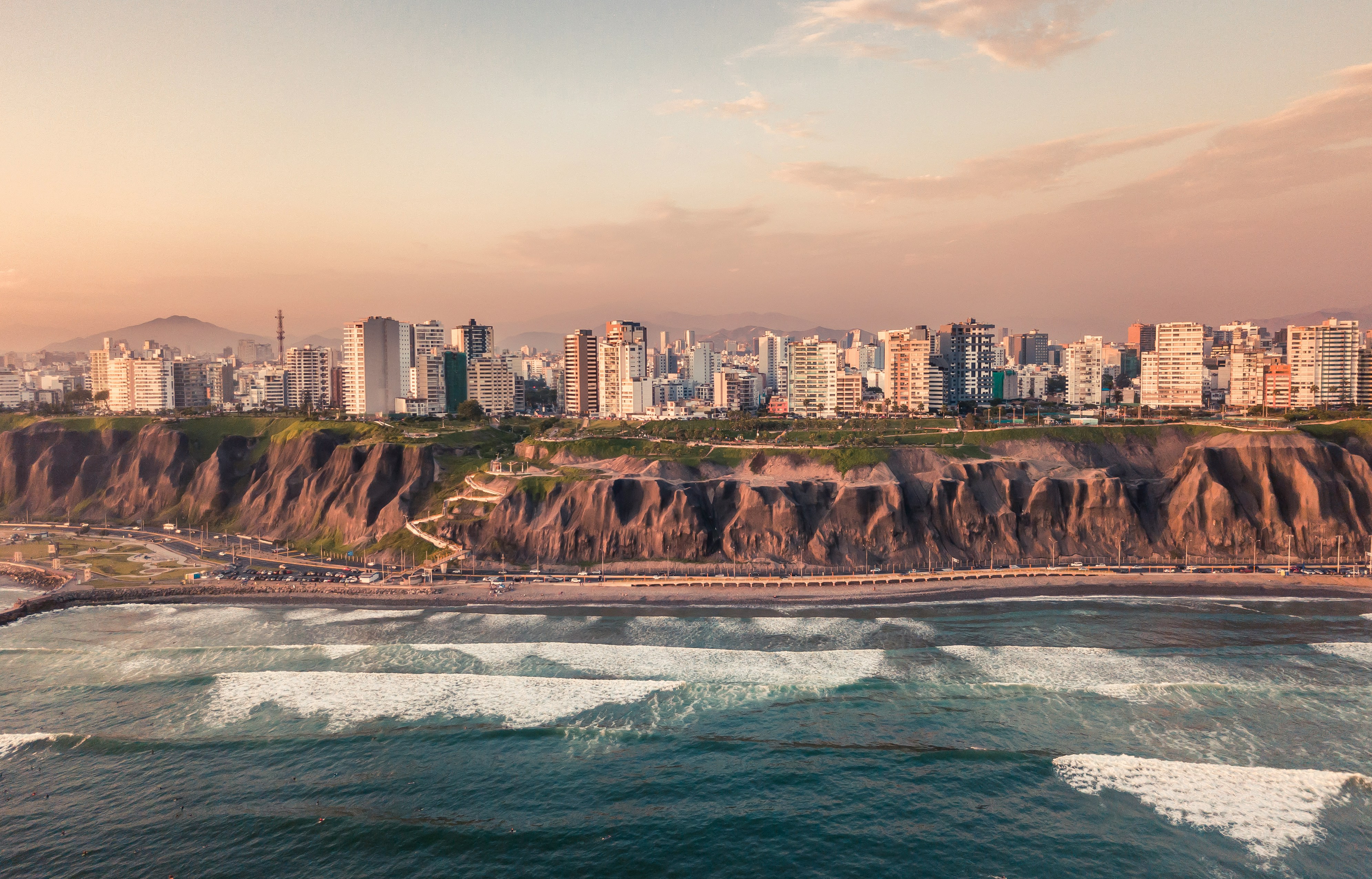 Miraflores coastline with ocean waves and Lima city skyline at dusk