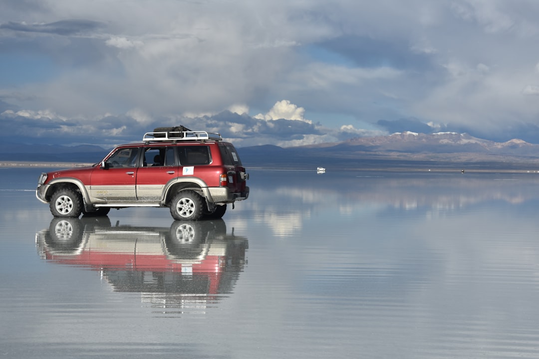 A 4WD vehicle on the flooded Uyuni Salt Flats in Bolivia, reflected in still water under storm clouds