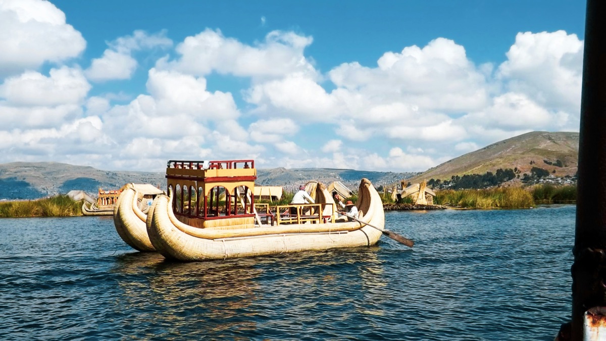 Traditional totora reed boat on Lake Titicaca with Puno in the background, Peru
