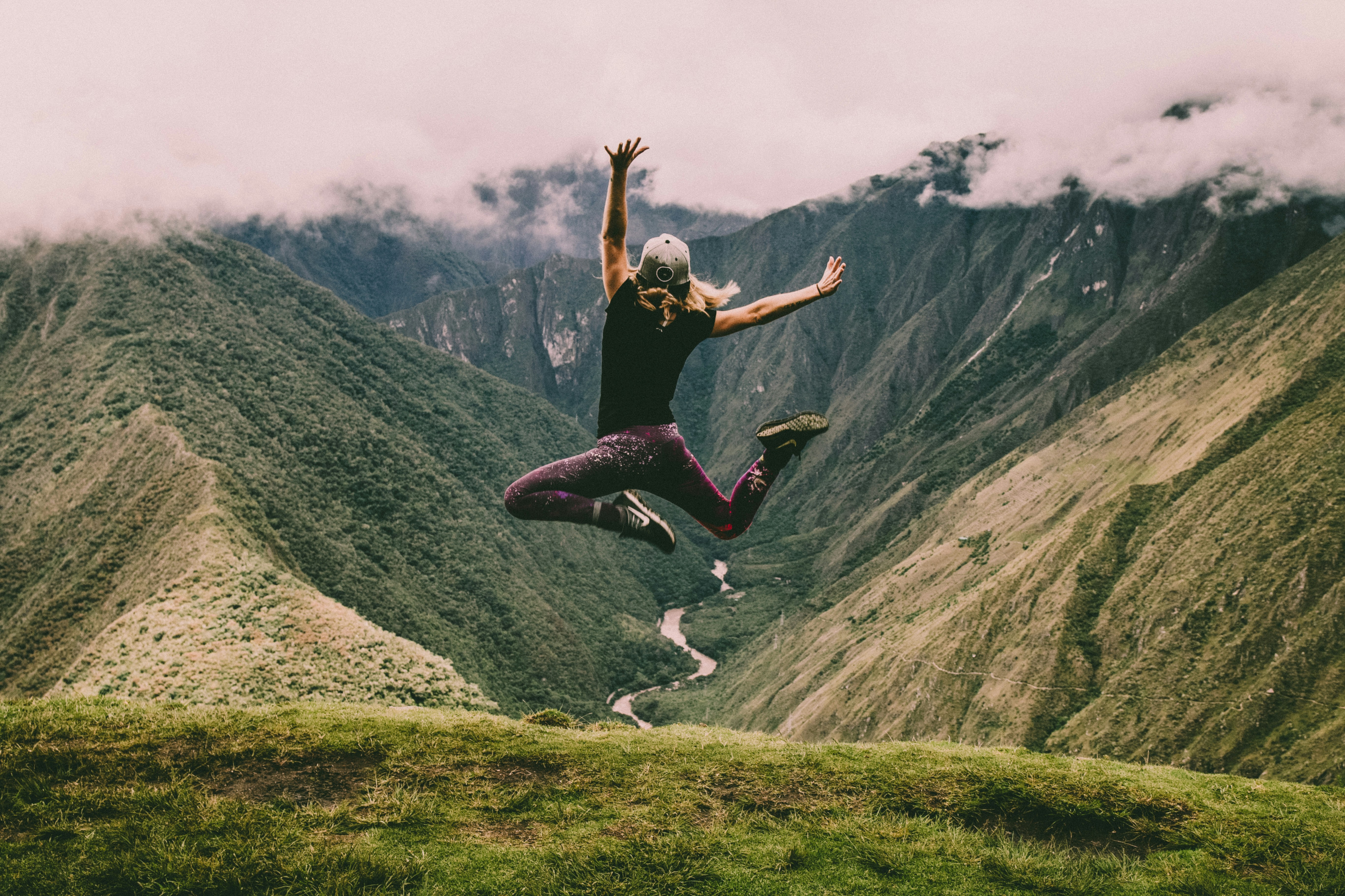 Hiker jumping on lush green Andean mountains after the wet season, Peru