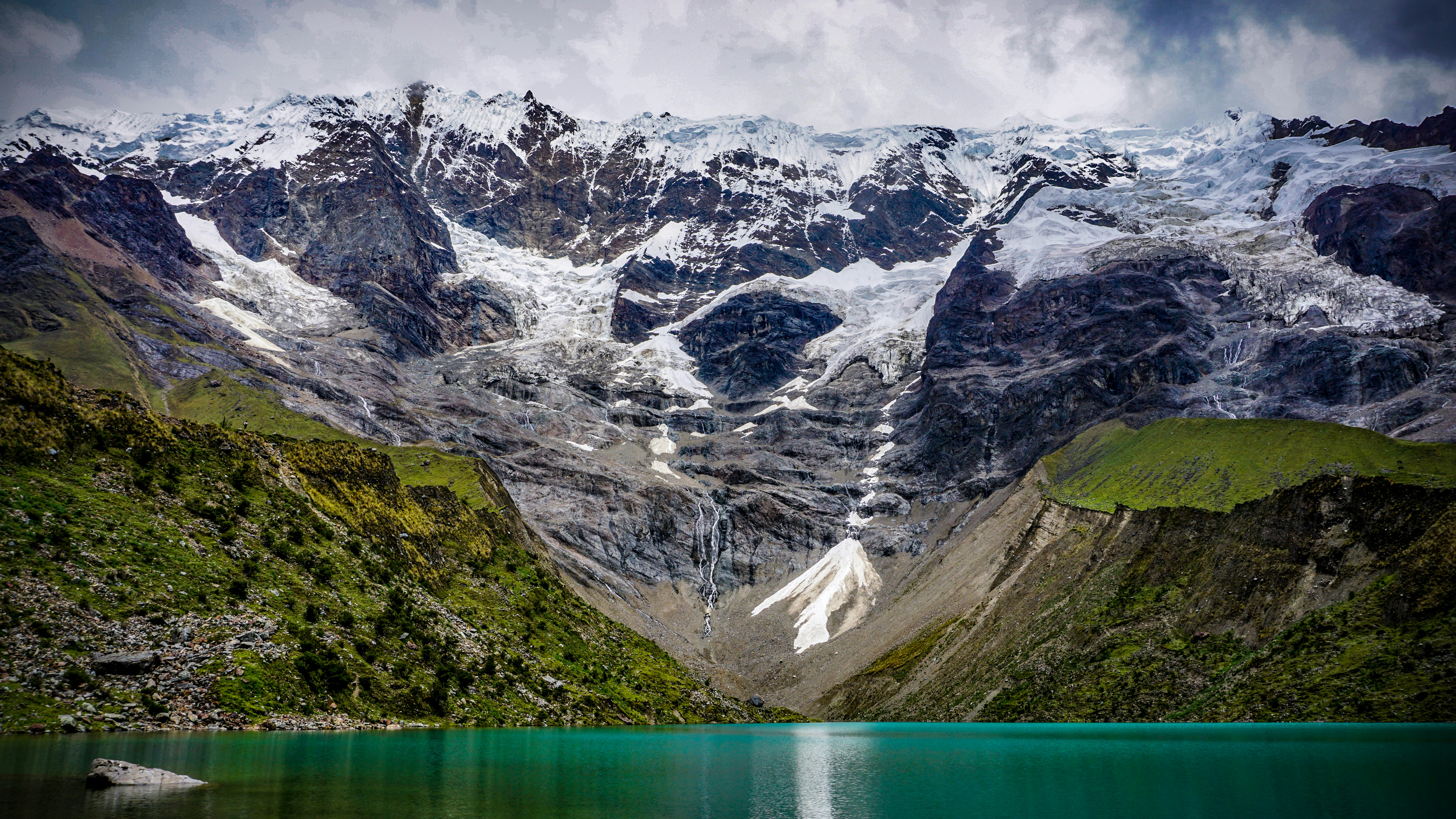 Turquoise glacial lake below snow-covered Andean peaks — high-altitude Peru trekking terrain