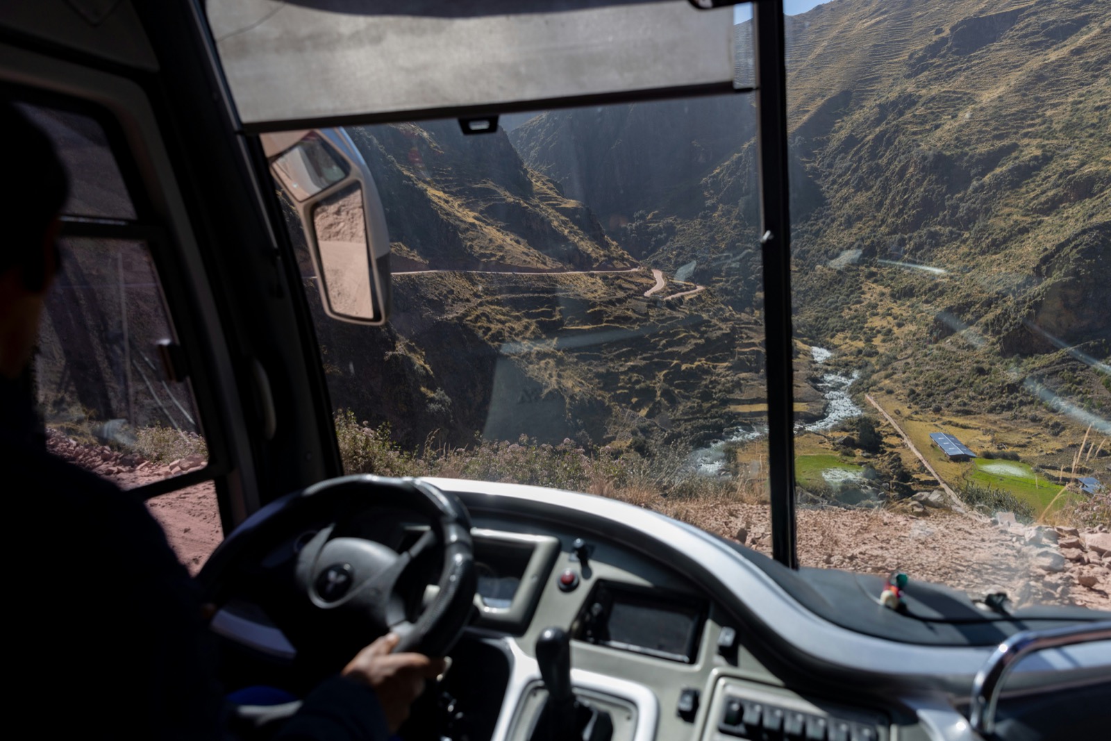 Bus driver navigating a winding mountain road through an Andean canyon, Cusco region, Peru