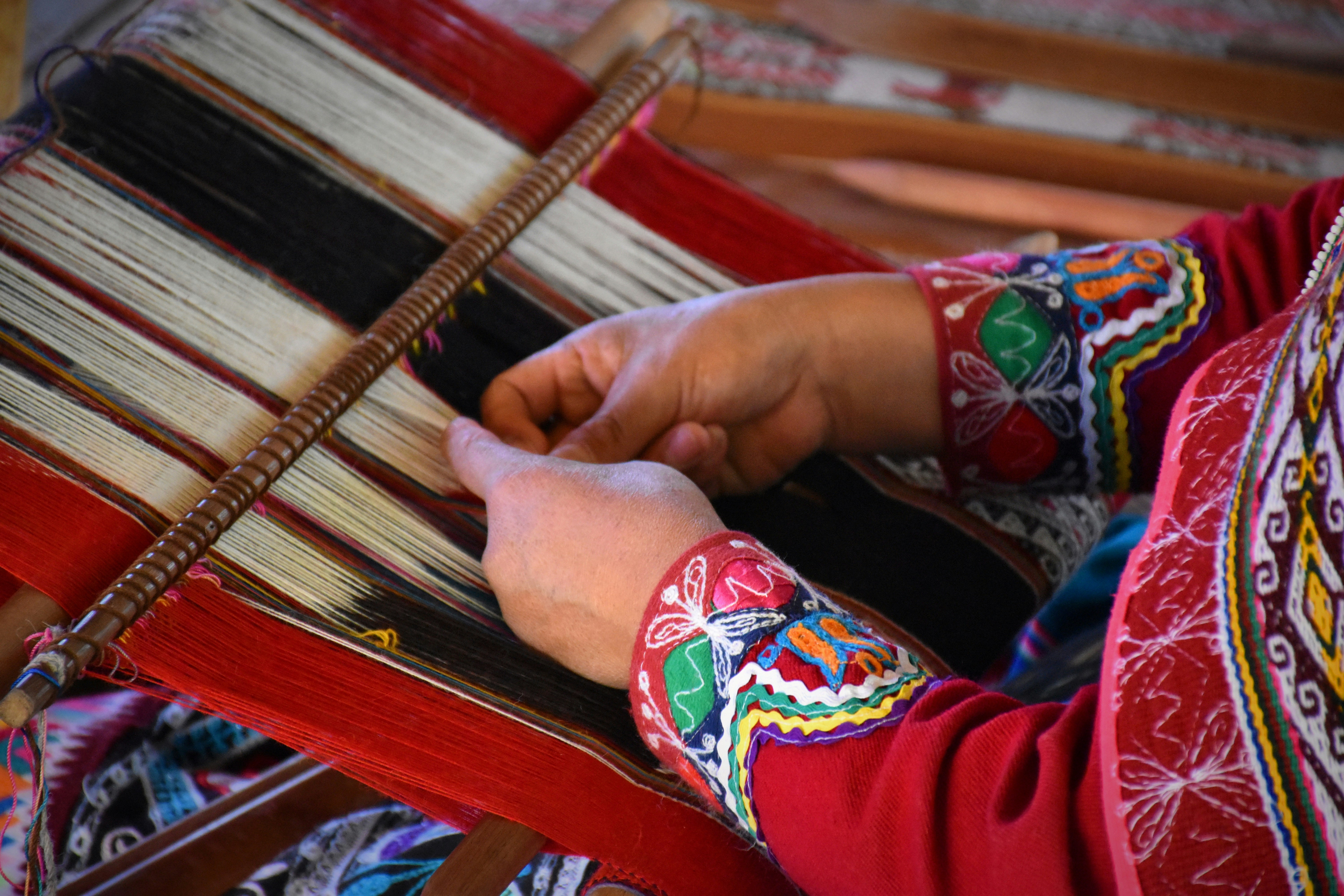 Peruvian woman weaving traditional colourful textiles at a market stall, Sacred Valley Peru