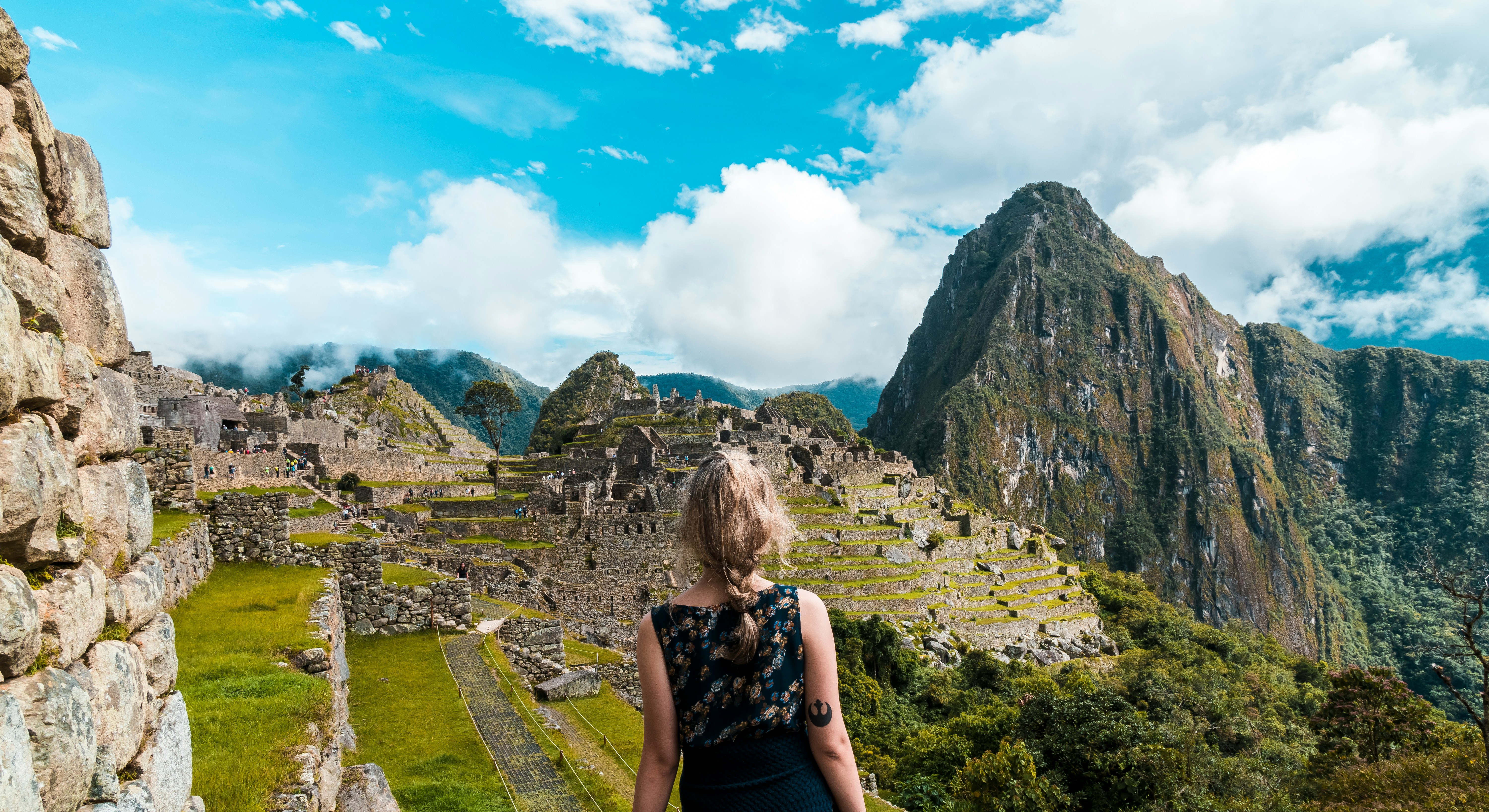 Solo female traveller standing at the entrance gate to Machu Picchu, looking out over the Inca ruins with Huayna Picchu peak rising behind