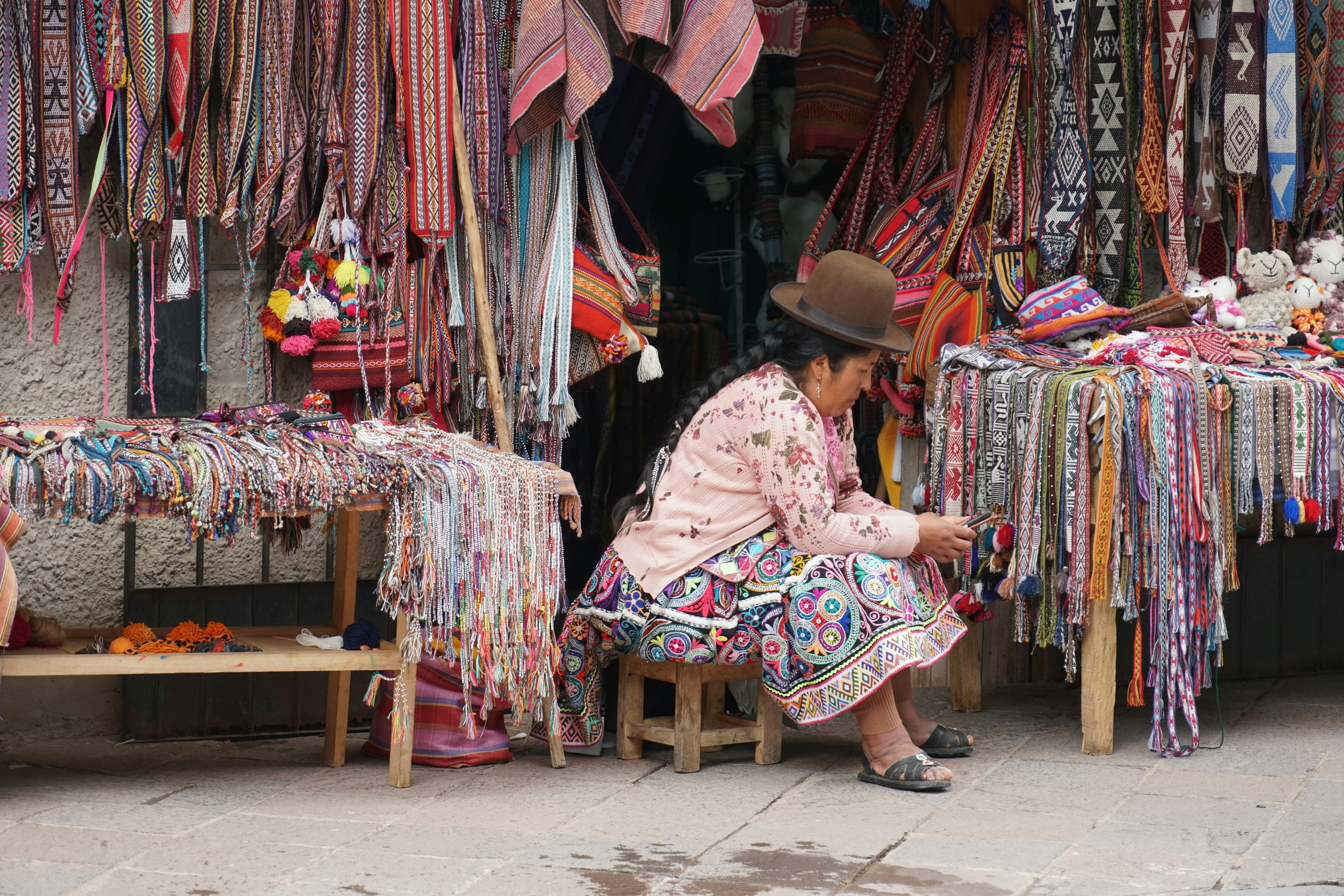Andean woman in traditional dress selling colourful textiles at Pisac market, Sacred Valley, Peru