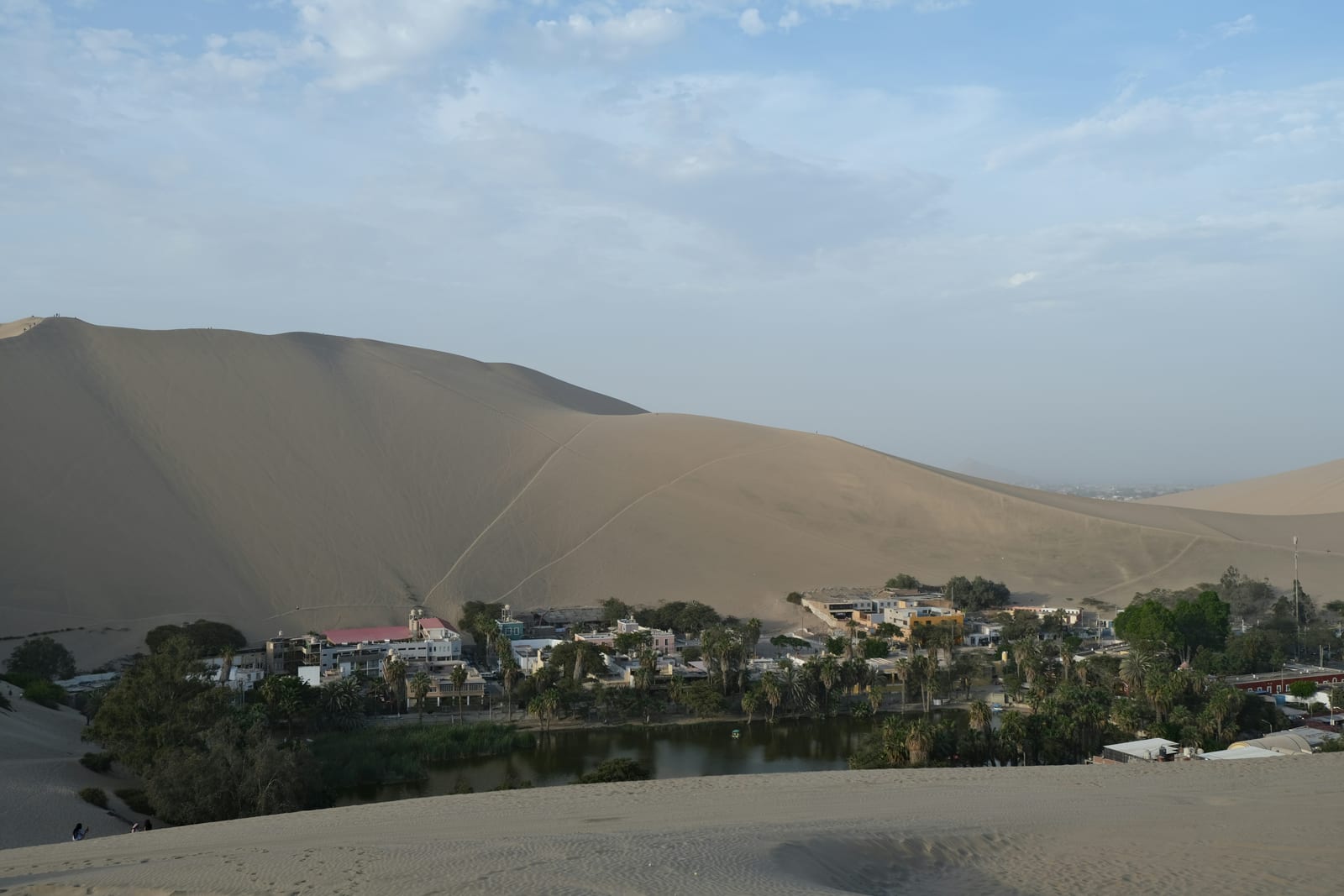 Huacachina oasis with palm trees and buildings at the foot of massive sand dunes, Ica, Peru